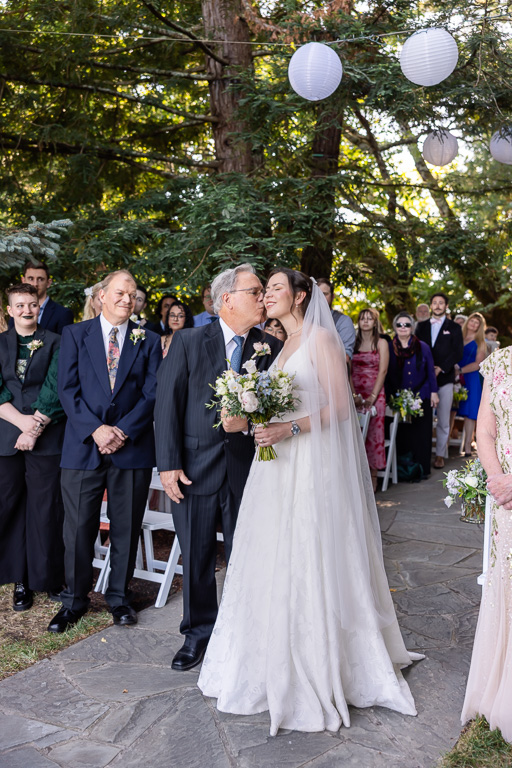 father of the bride giving her a kiss at the end of the aisle