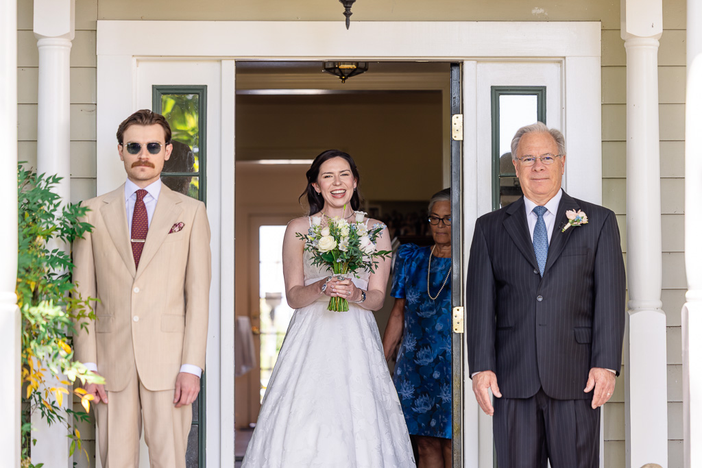 bride walking out of a door for her first look with both dad and brother