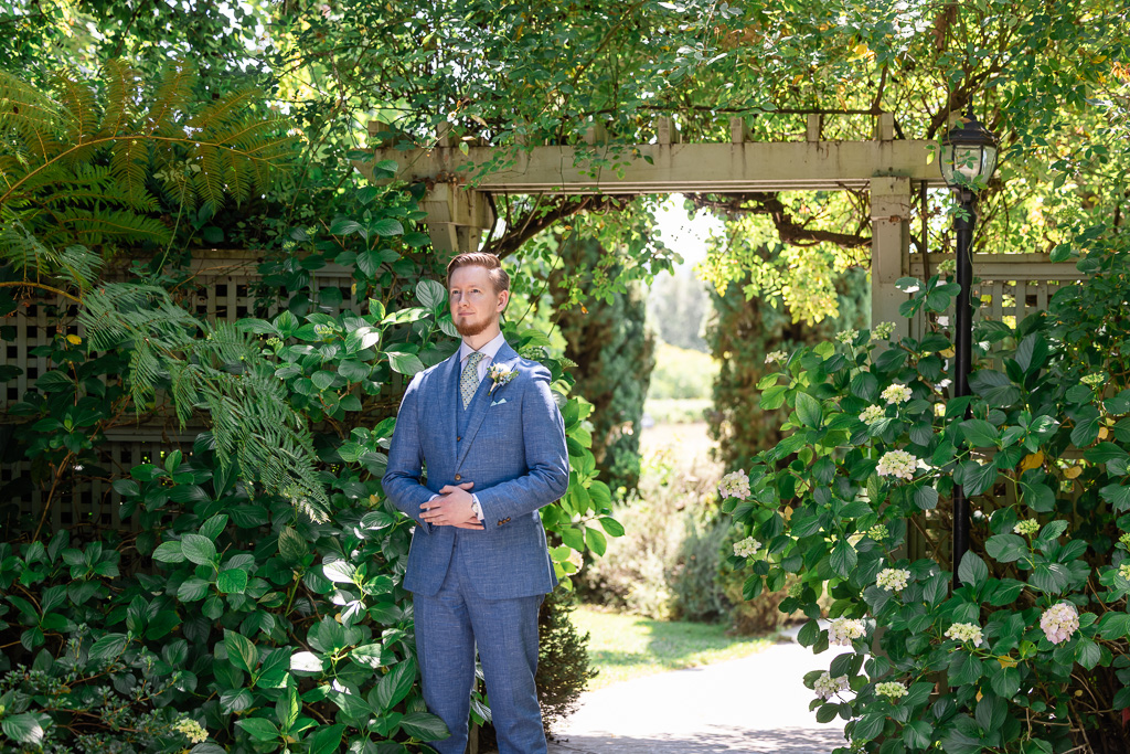 groom standing at garden entrance waiting for first look