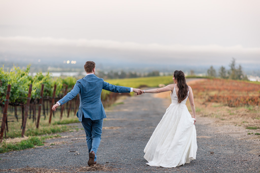 fun candid photo of bride and groom walking down the road next to some vineyards