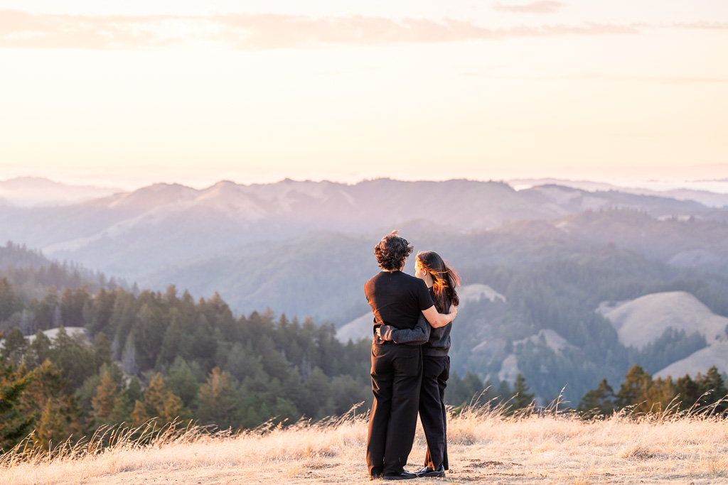 couple standing arm in arm on a mountain at sunset