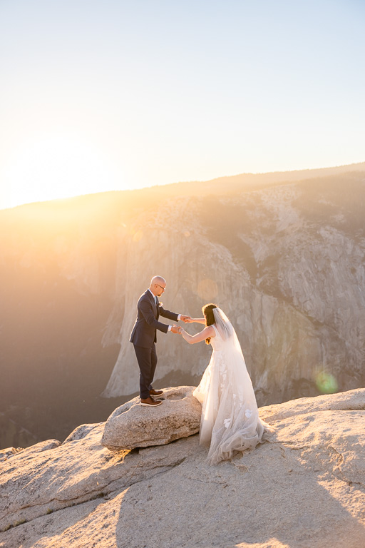 groom helping bride up onto a rock at an overlook