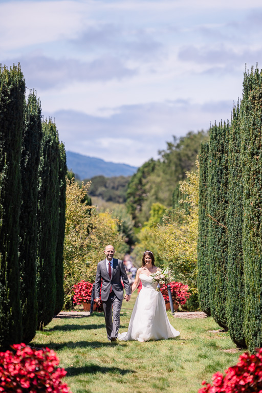 bride and groom walking down a very long garden aisle together