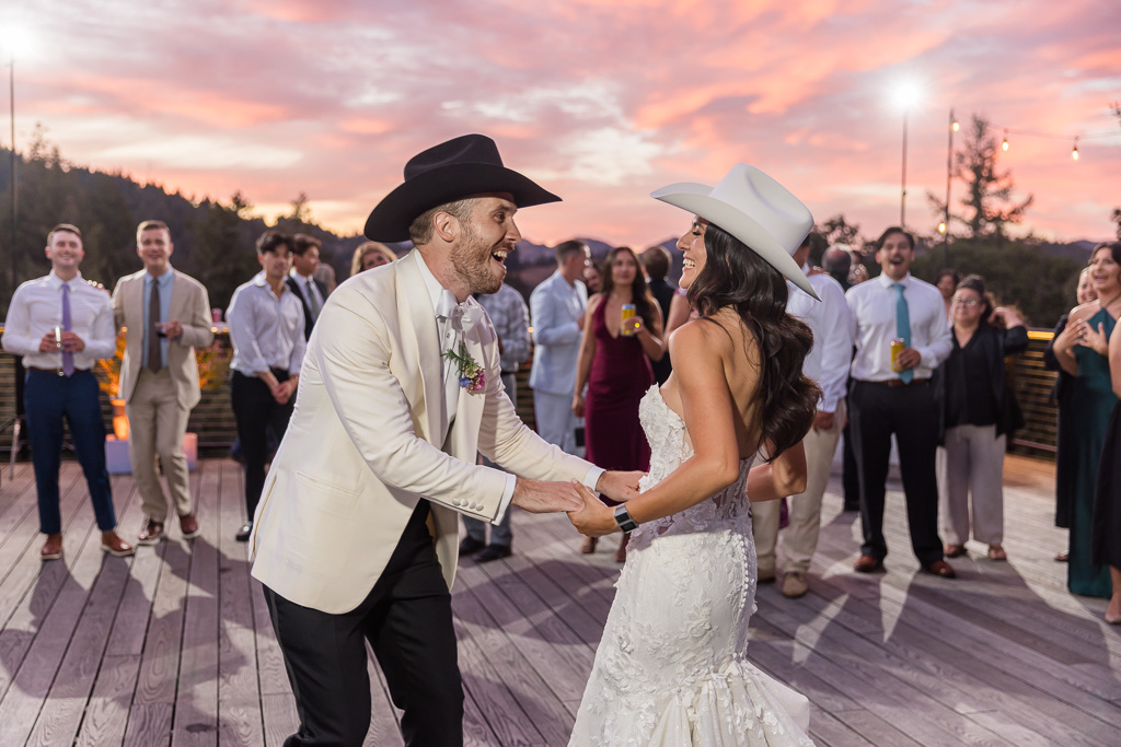 bride and groom dancing in cowboy hats under a spectacular pink sunset sky