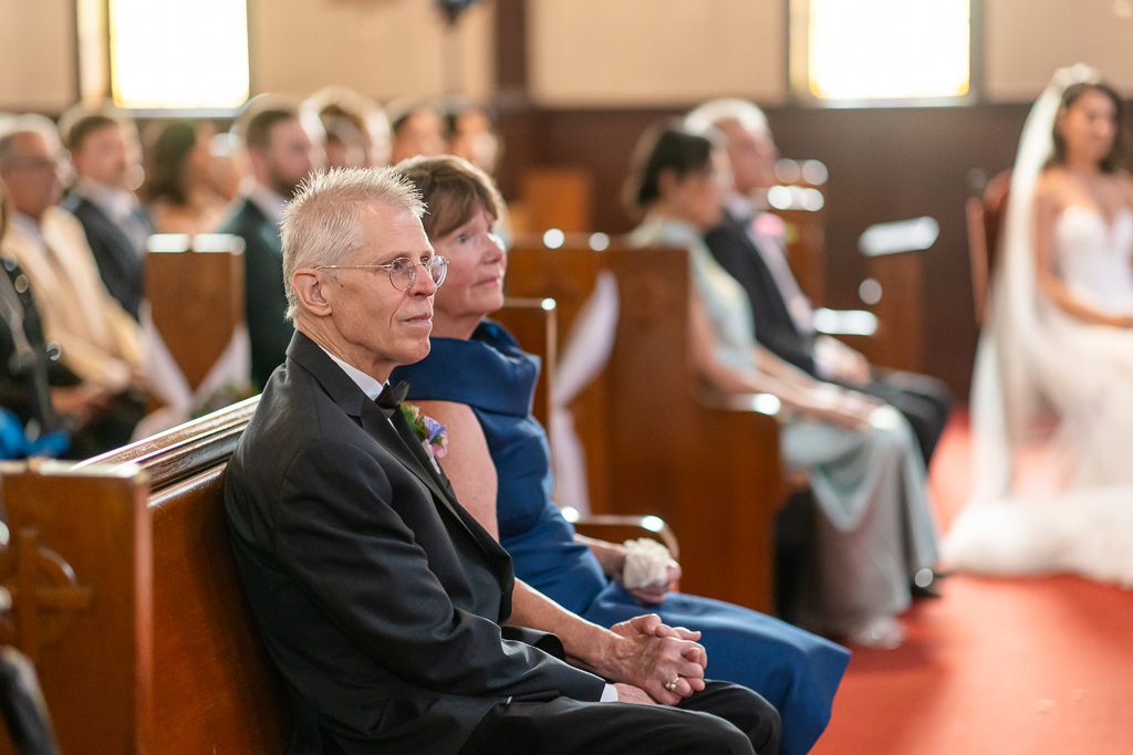 parents of the groom seated in the front pew and holding hands