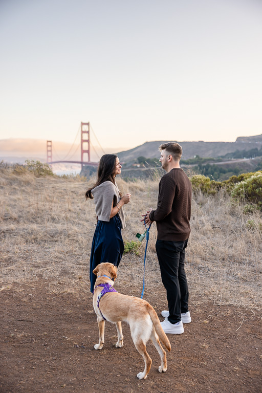 couple and their dog on a trail with the Golden Gate Bridge in the distance