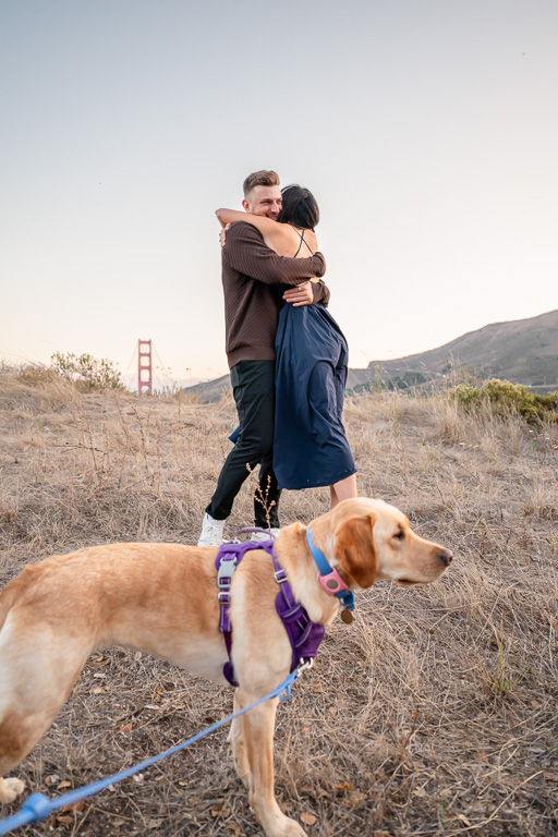 couple hugging as their dog photobmbs them