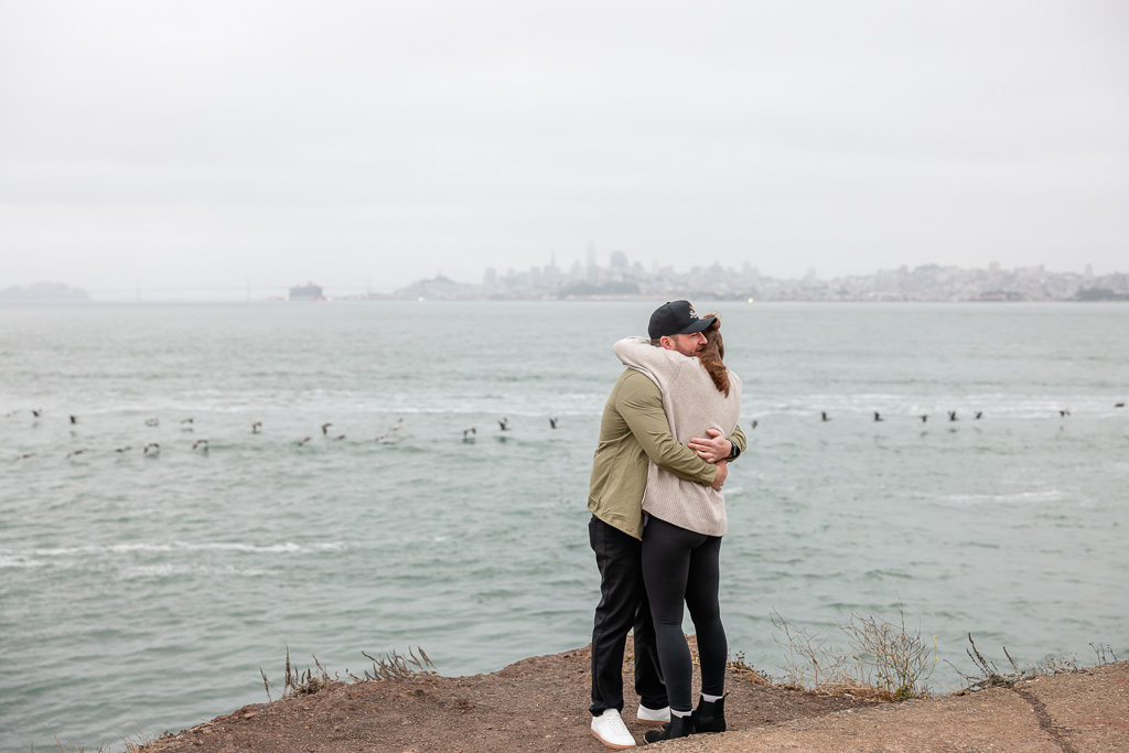 couple hugging while seagulls flap across the water behind them