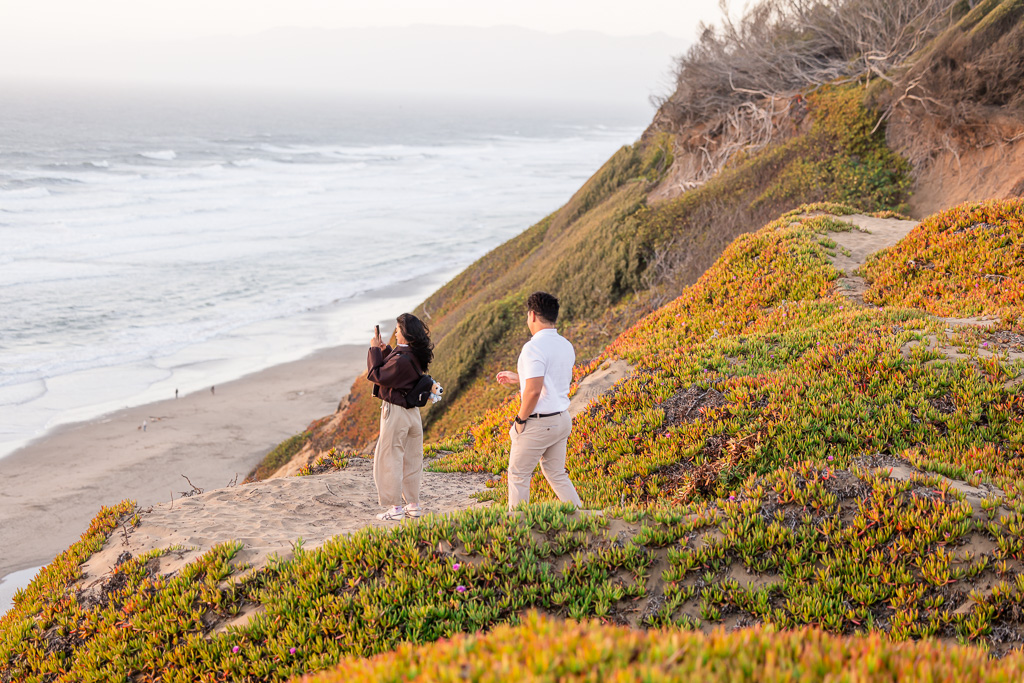 man walking up behind his girlfriend to surprise her with a ring