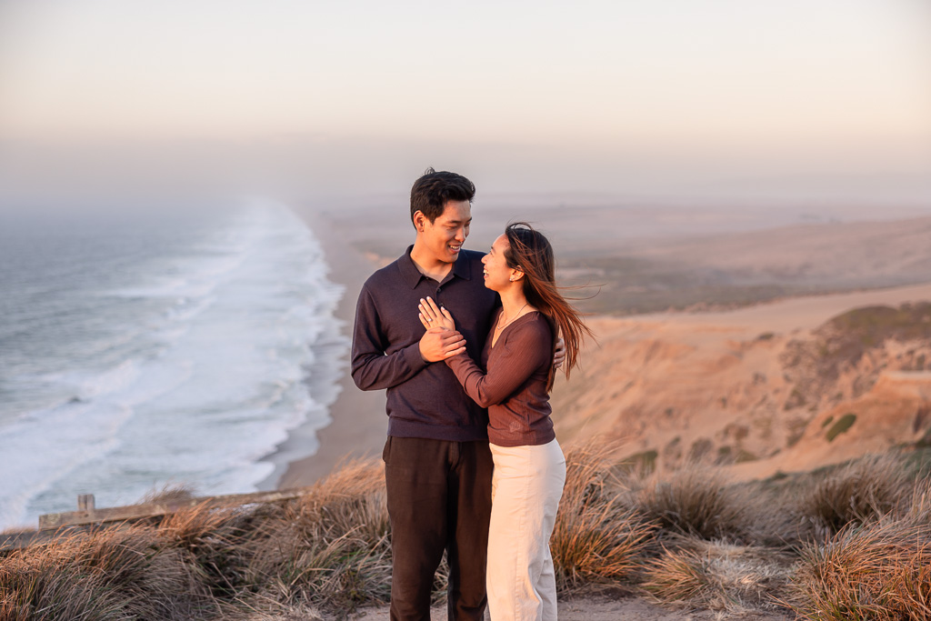 The newly engaged couple share a close embrace in the warm sunset light at Point Reyes.
