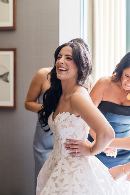 bride smiles as a bridesmaid helps with her wedding dress