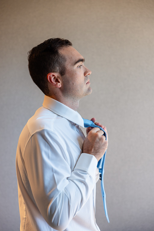 Groom adjusts his tie while getting ready for the wedding