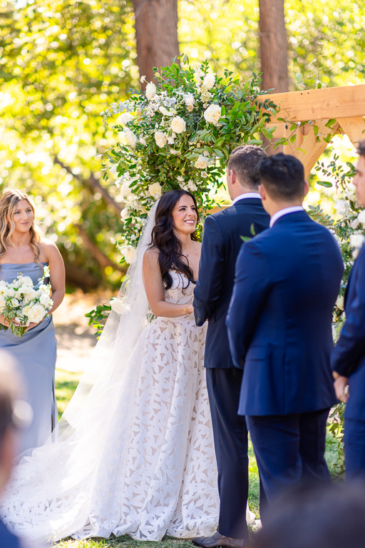 Bride and groom face each other at the Creekside Lawn with the wedding party nearby