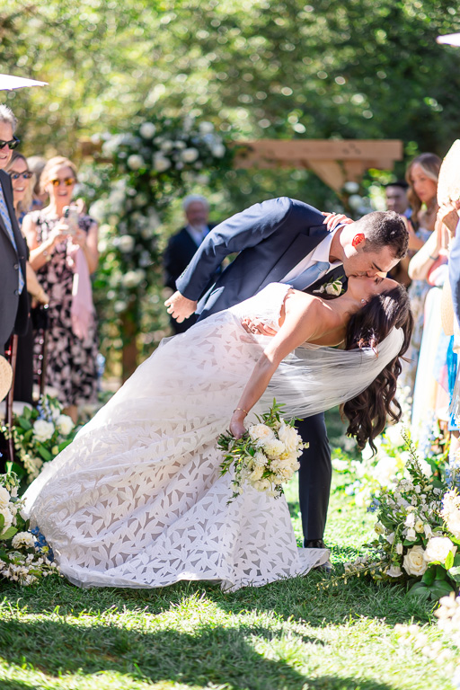 Groom dips and kisses the bride just after their outdoor ceremony in the Creekside Lawn