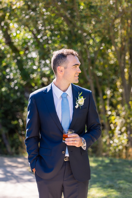 Groom holds a drink for a portrait among the trees