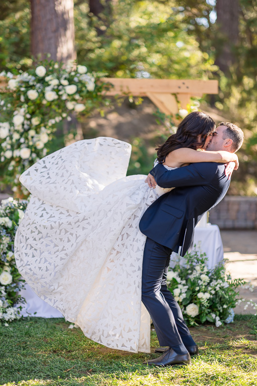 Groom lifts the bride in his arms beneath the floral arch