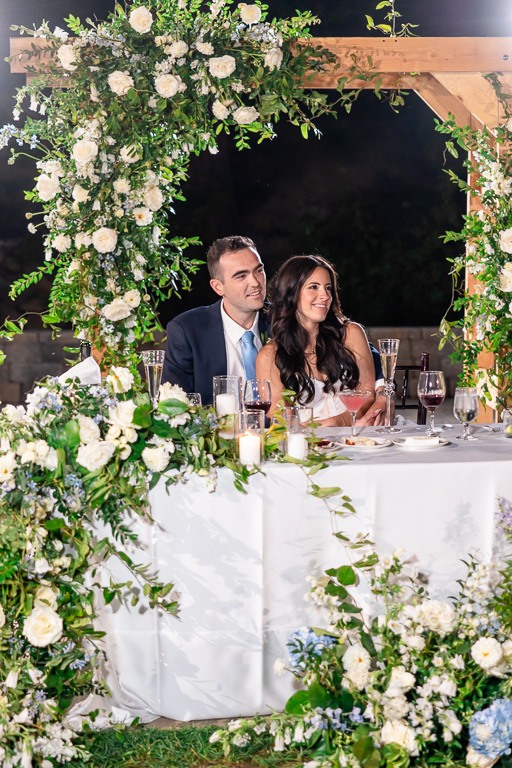 Bride and groom sit together beneath flowers at their reception table