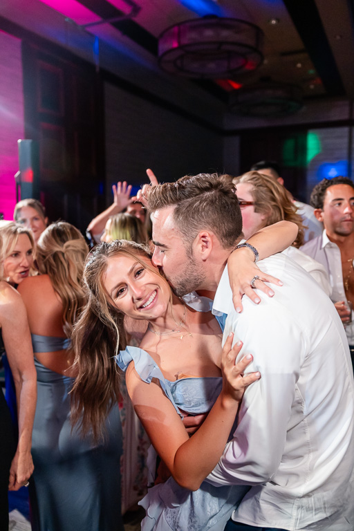 Wedding guests embrace on the dance floor beneath colorful lights