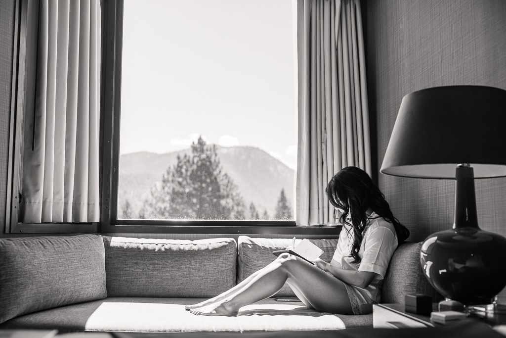 beautiful B&W shot of bride sitting writing her vows by a window with a Tahoe forest view