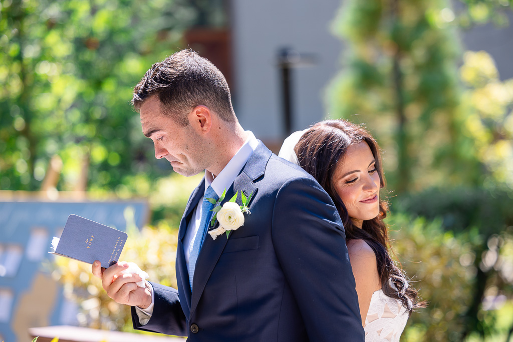 Groom reads his vows while standing back to back with the bride during outdoor first touch at the Water Gardens