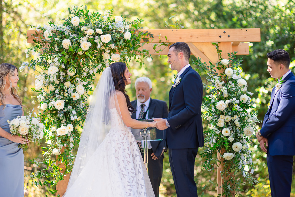 Bride and groom hold hands beneath the floral arch at Hyatt Regency Lake Tahoe Resort