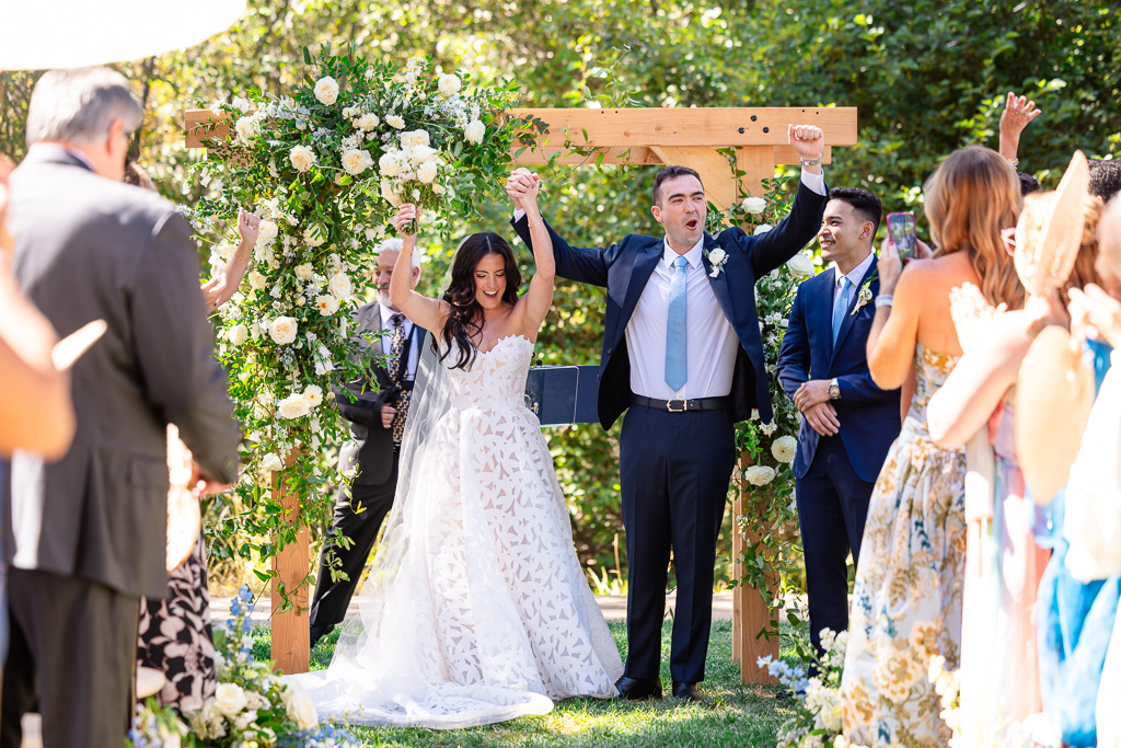 Bride and groom celebrate beneath the arch as guests cheer