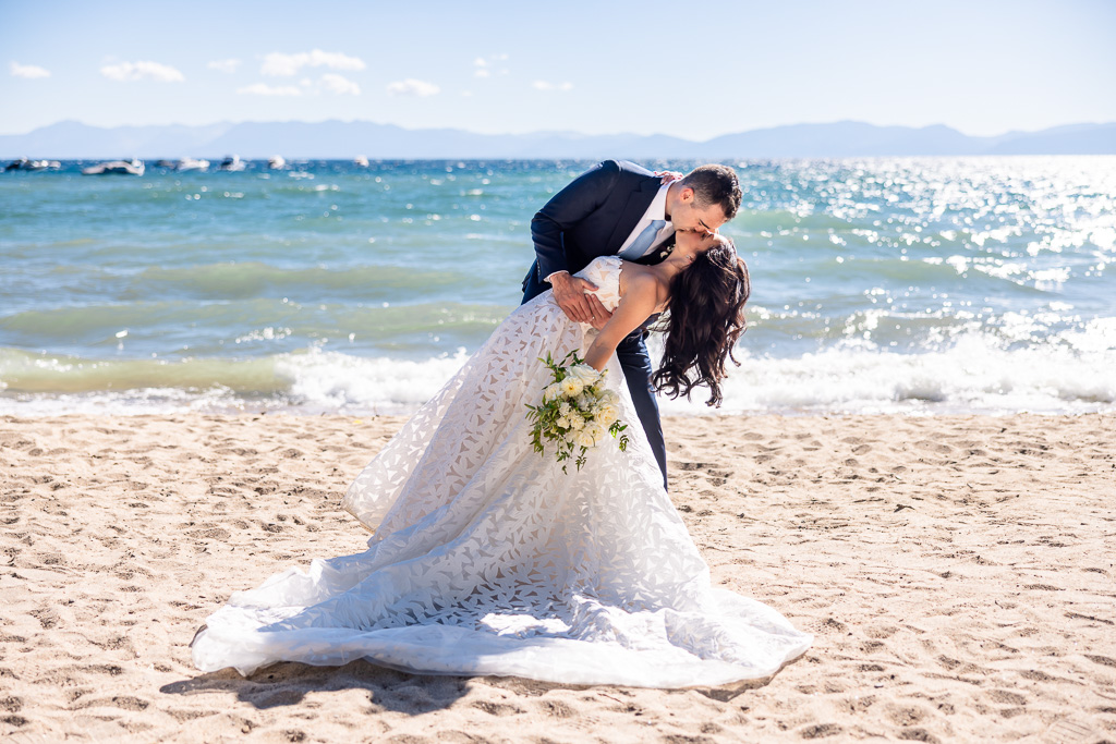 Bride and groom dip & kiss at the shore for Lake Tahoe wedding portraits