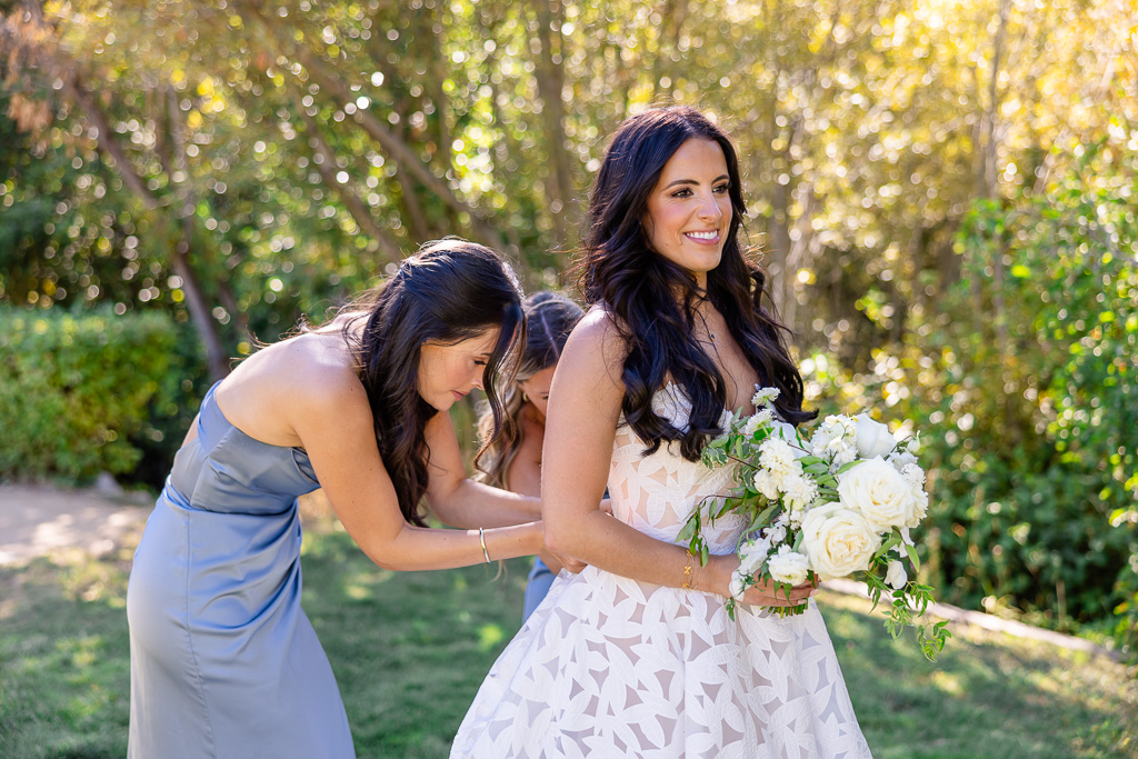 Bridesmaid adjusts the back of the bride’s wedding dress