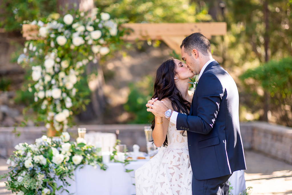 Bride and groom share a kiss beneath the floral arch at the end of their first dance