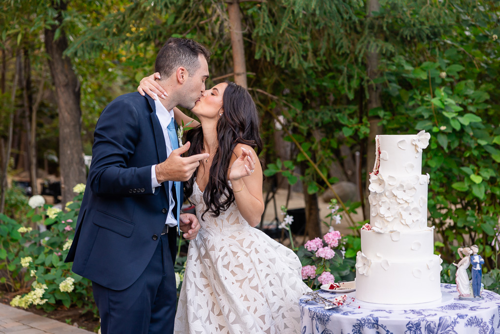 Bride and groom kiss beside their wedding cake
