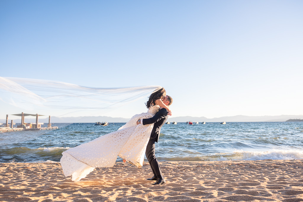 Groom lifts the bride as waves break along Lake Tahoe