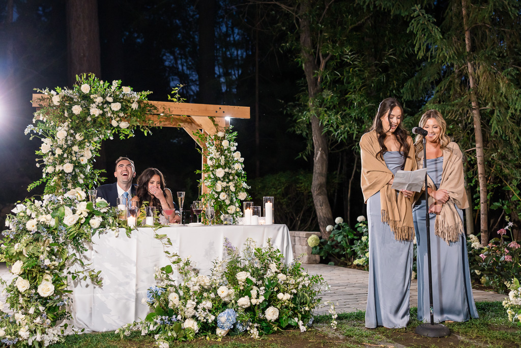 Two bridesmaids deliver a joint toast beside the newlyweds