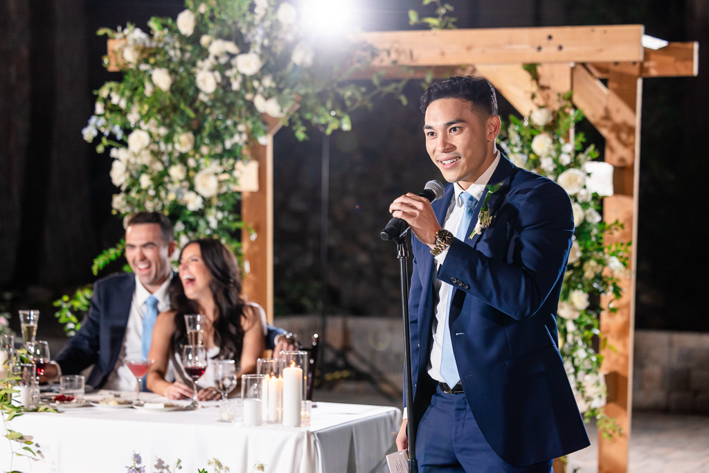 Wedding guest speaks at the reception microphone beside the newlyweds