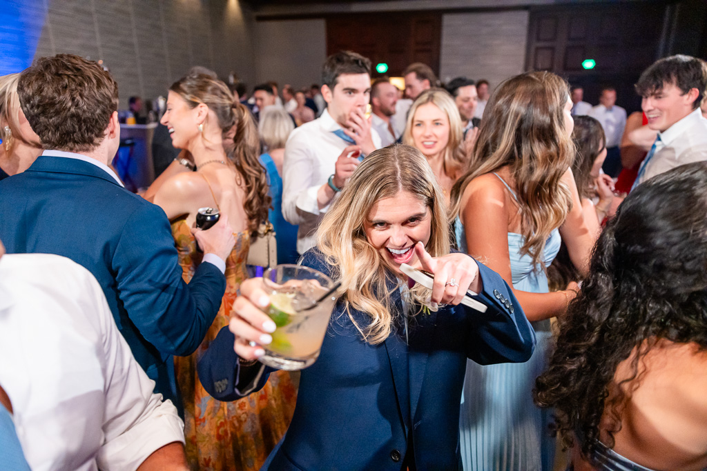 Wedding guest dances while holding a drink on the reception floor