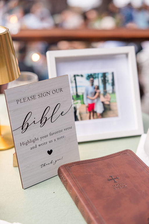 Bible guestbook and framed photo beside a sign inviting guests to highlight a favorite verse and leave a note.