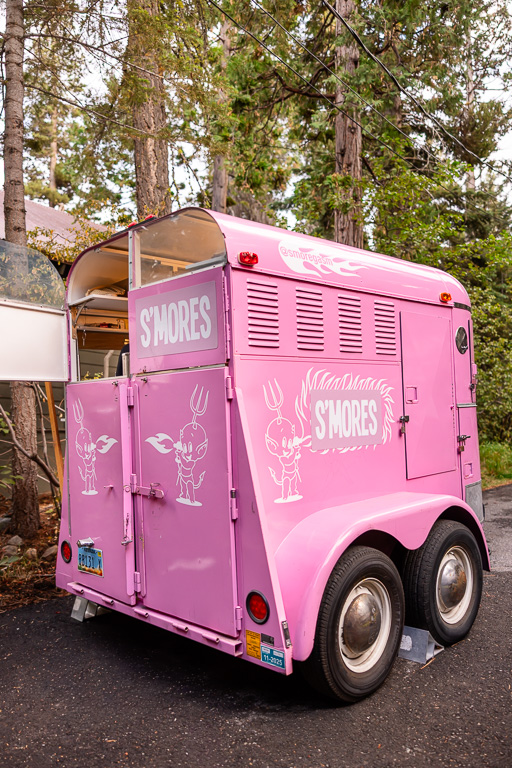 Pink s’mores trailer parked among tall pines for the pre-wedding celebration.