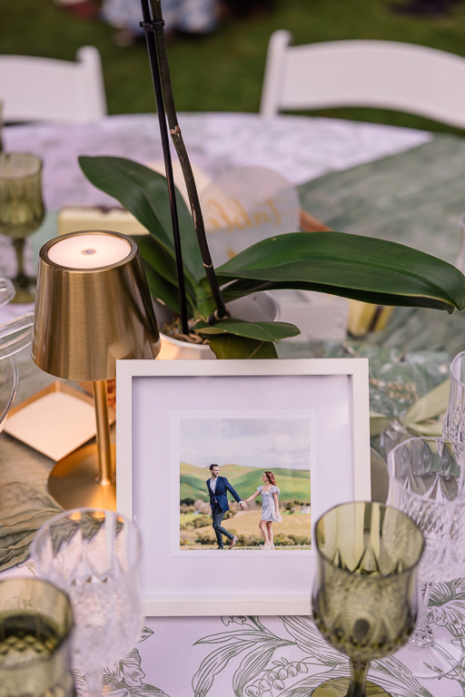 Reception table detail with an orchid, candle, green goblets and a framed photo of the couple.