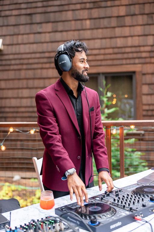 A DJ in a burgundy jacket works the turntables at the outdoor party.