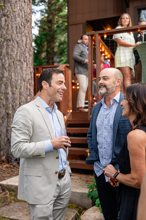 The father of the bride chats with a guest beside one of the pines.