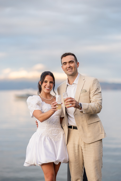 Bride and groom in front of a sunset sky at Lake Tahoe holding champagne glasses