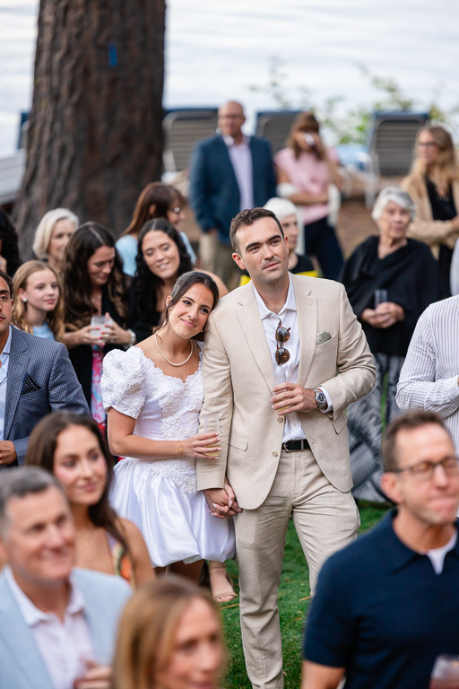 The bride and groom stand hand in hand among their guests during speeches