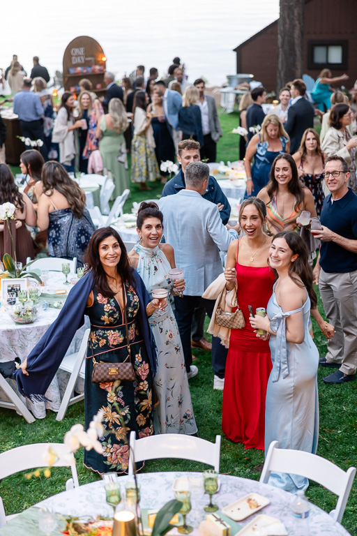 Guests gather around outdoor tables on the lawn beneath the pines.