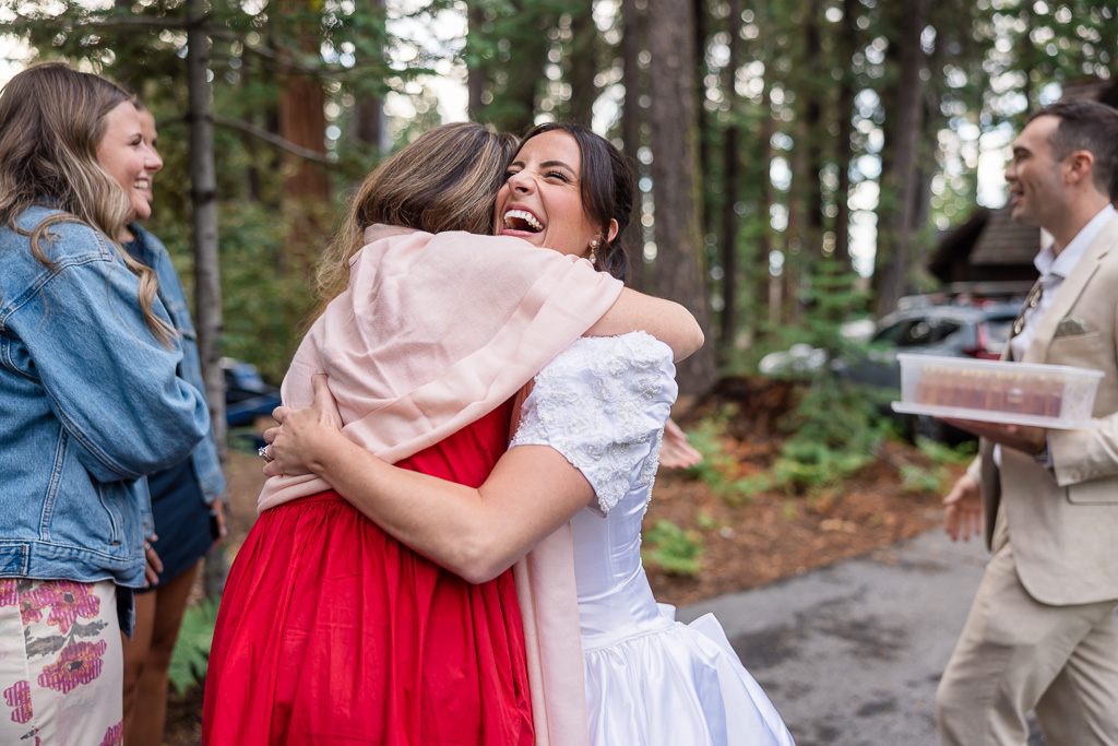 The bride hugs a friend in a red dress as guests gather nearby.