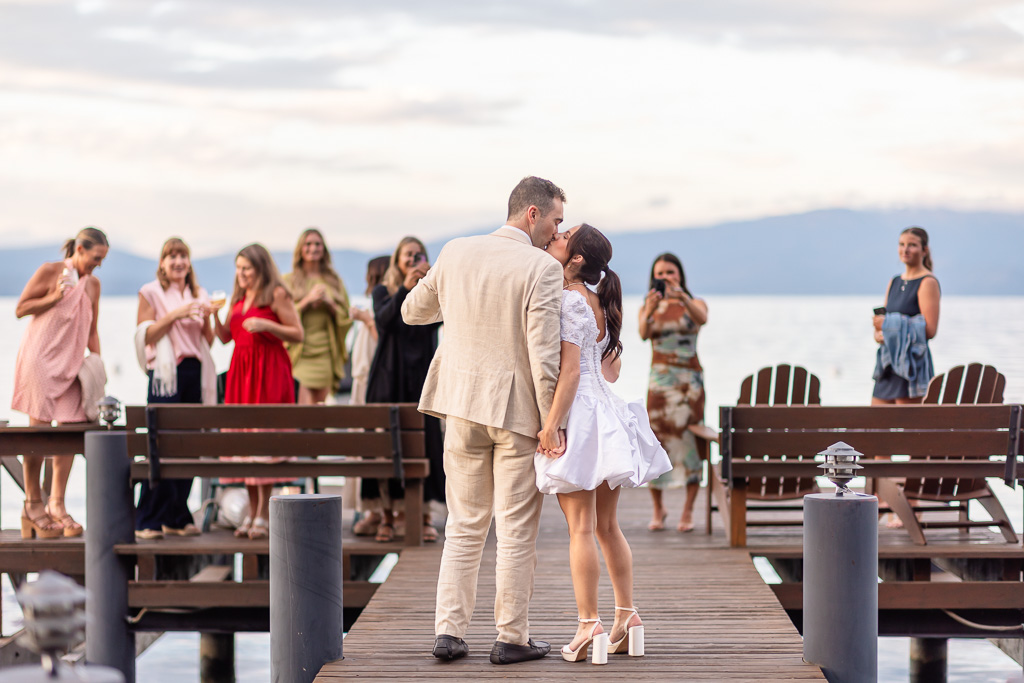 The couple kisses on the dock while friends look on
