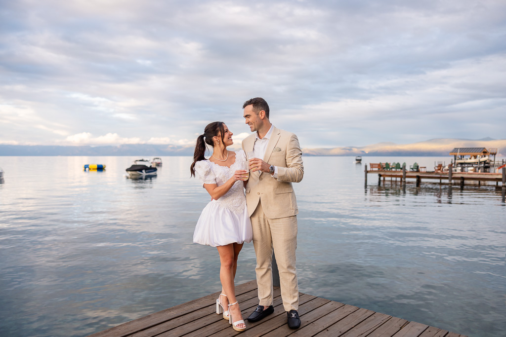 The couple poses hand in hand at the end of a Tahoe dock, with mountains across the water.