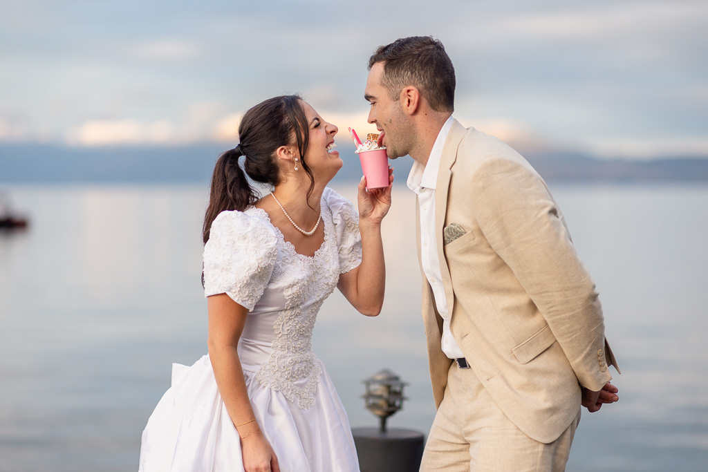 The bride offers her groom a pink drink on the dock.