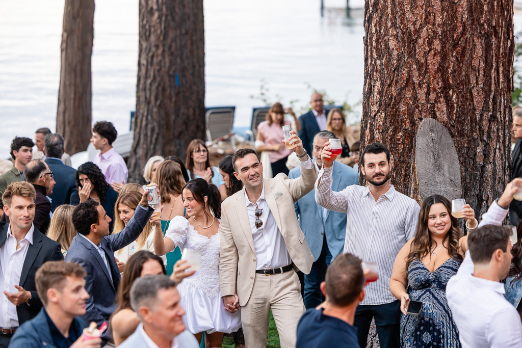 The bride and groom cheer with family and friends beneath the pines at their Tahoe lakeside gathering.