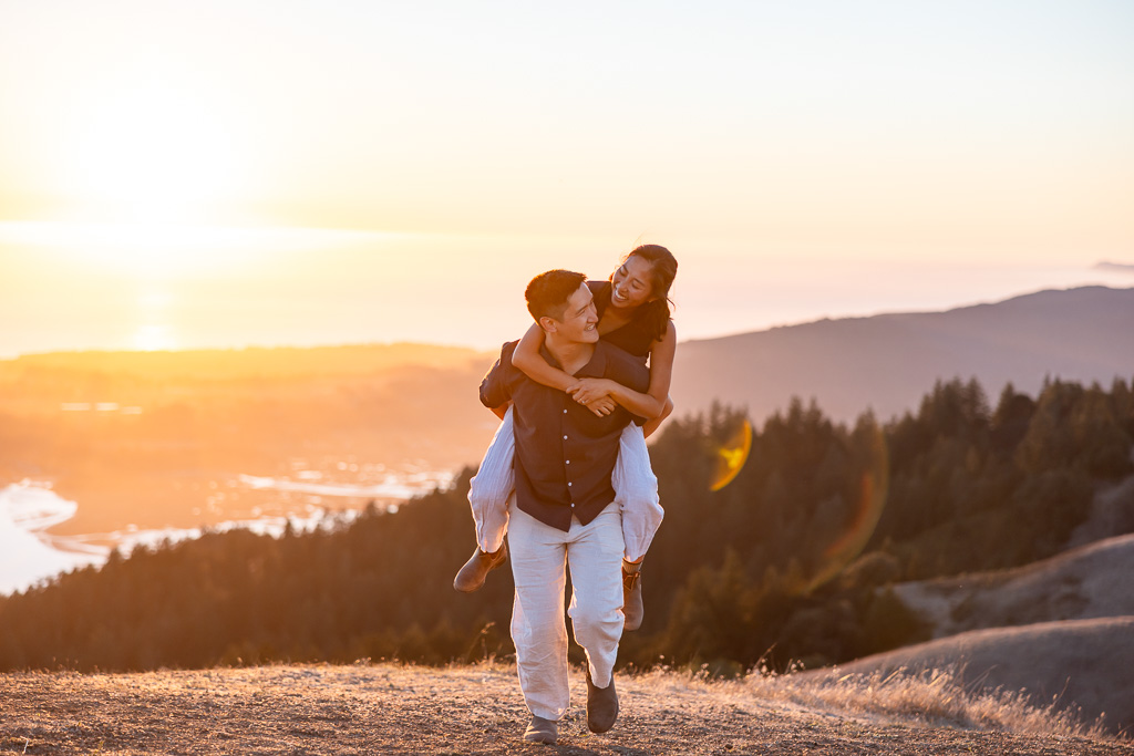 Piggyback ride as couple laughs against the glowing sunset and coastal hills.
