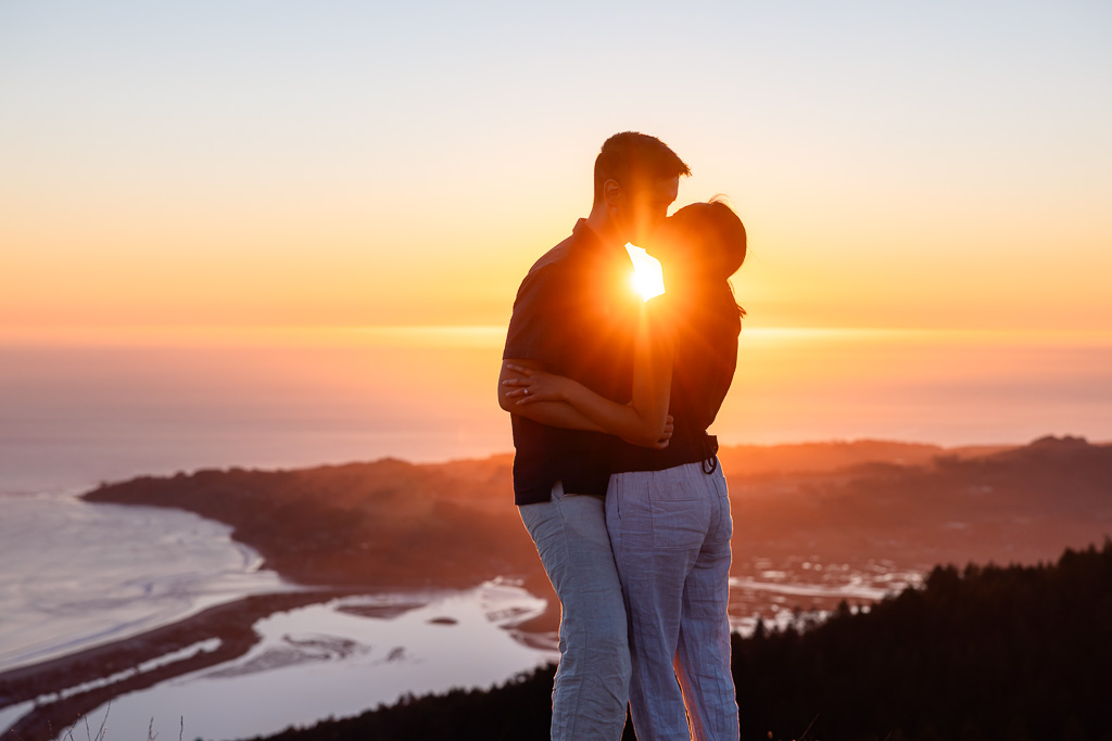 A couple kisses at sunset, their silhouette framed by the ocean and the coastline below Mount Tamalpais.
