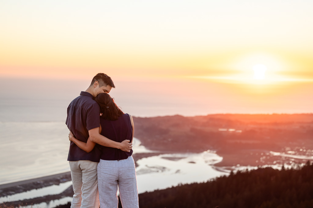 The couple stands close together, looking out over the ocean and Stinson Beach at sunset.